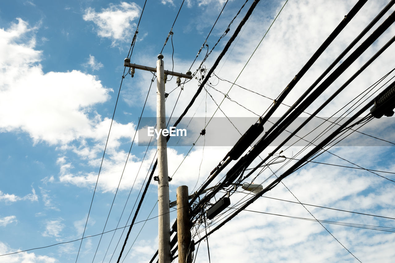 Low angle view of electricity pylons against cloudy sky