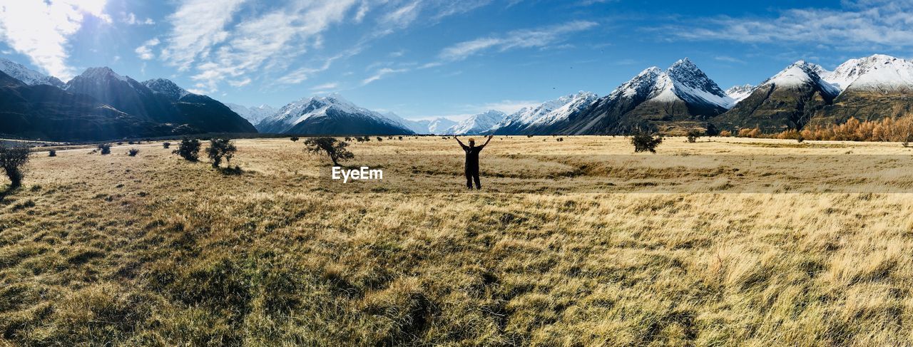 Man with arms raised on field against snowcapped mountains 