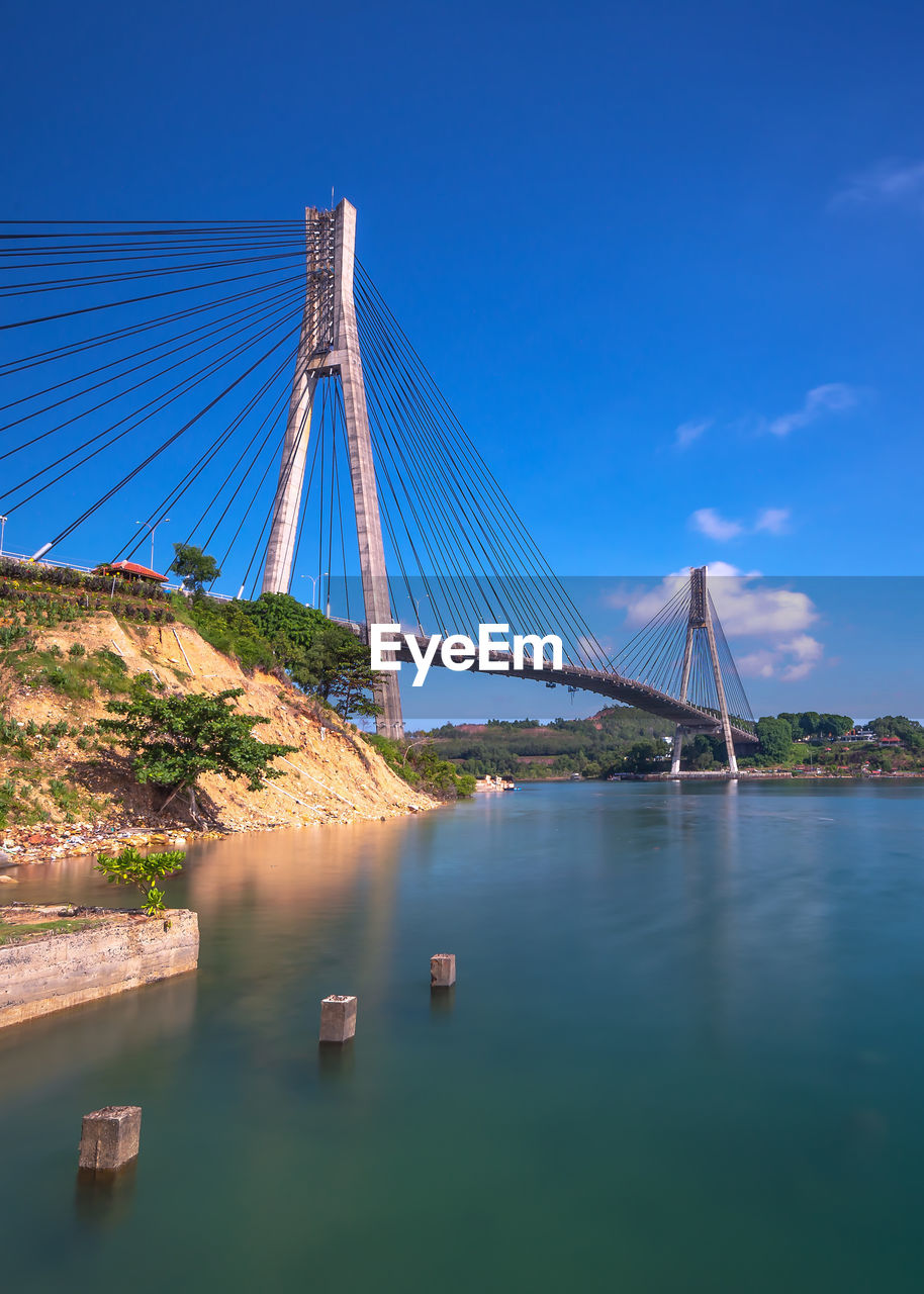 SUSPENSION BRIDGE OVER RIVER AGAINST BLUE SKY