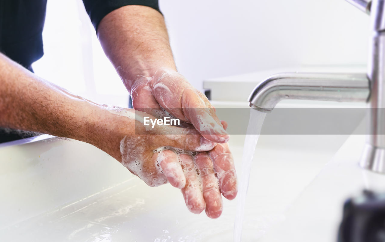 MIDSECTION OF MAN MAKING FACE WITH WATER IN BATHROOM