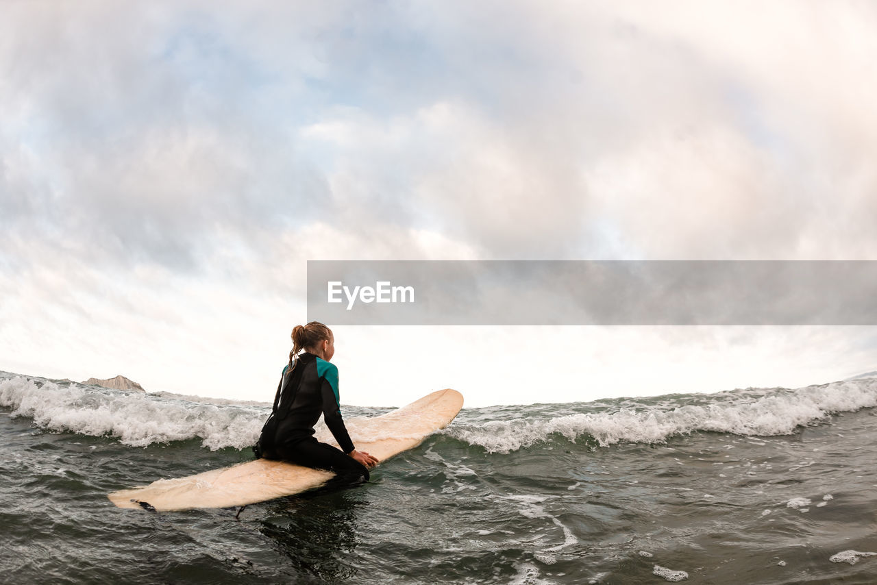 Adolescent girl looking away sitting on a surfboard in the ocean