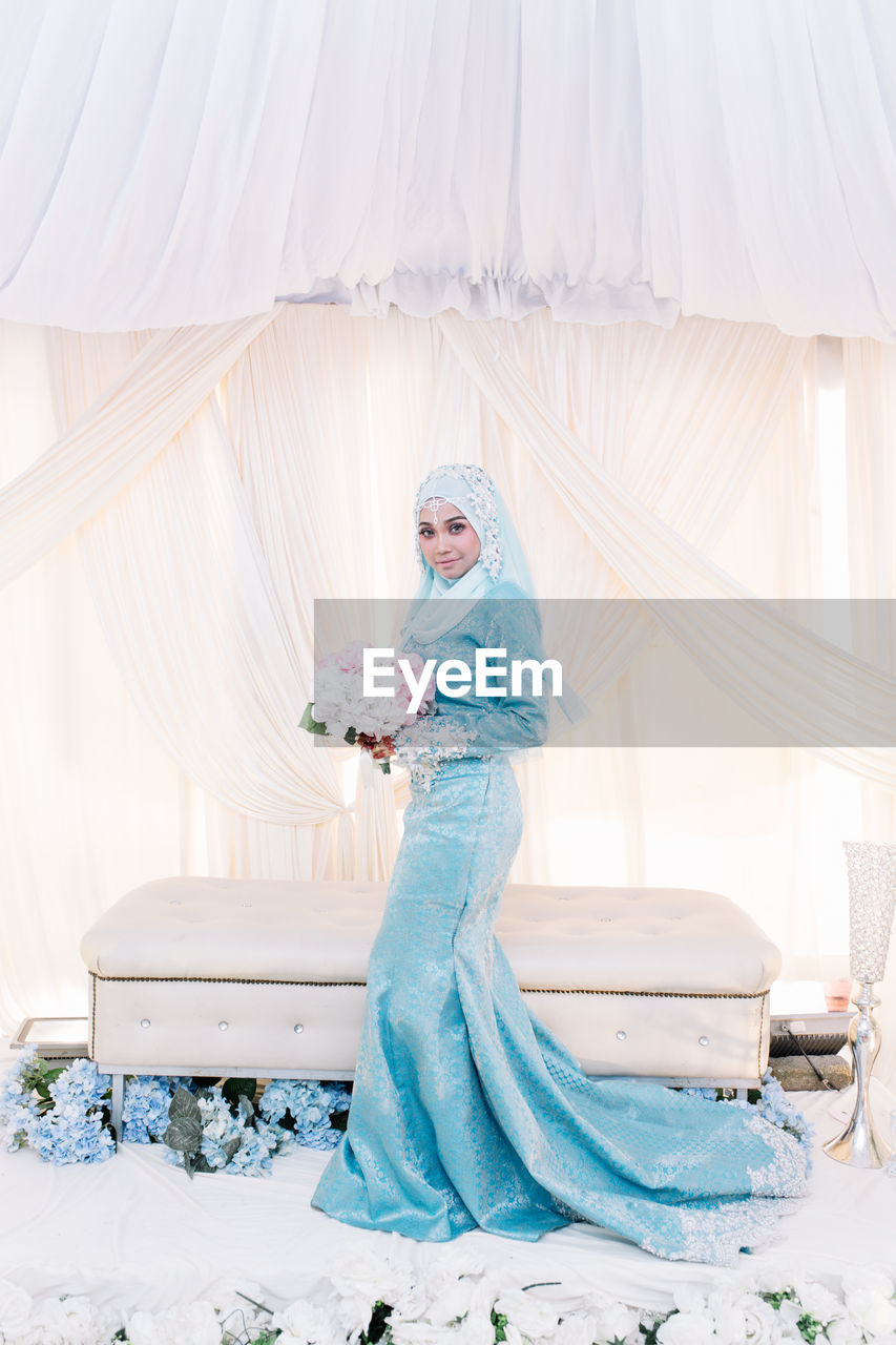 Portrait of smiling bride standing against curtain