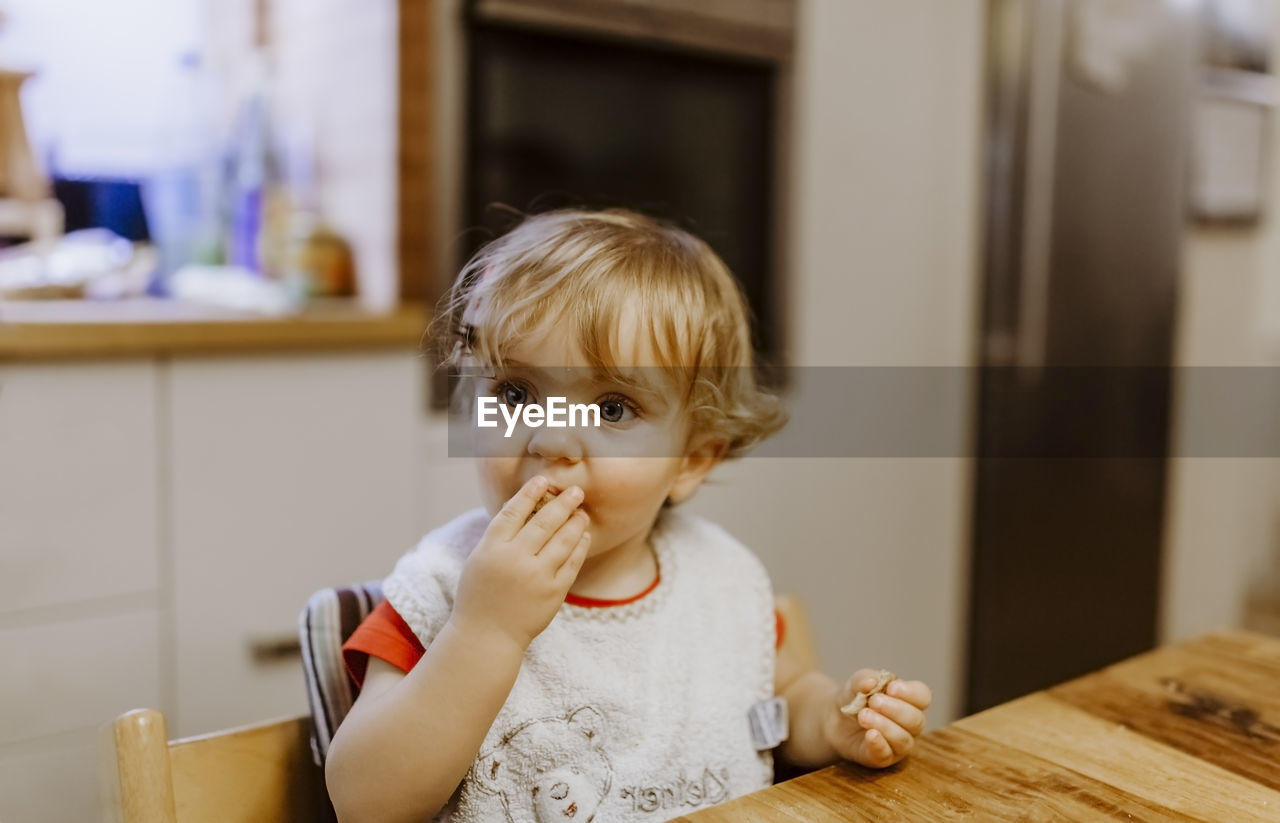 Cute baby boy sitting by table on chair at home