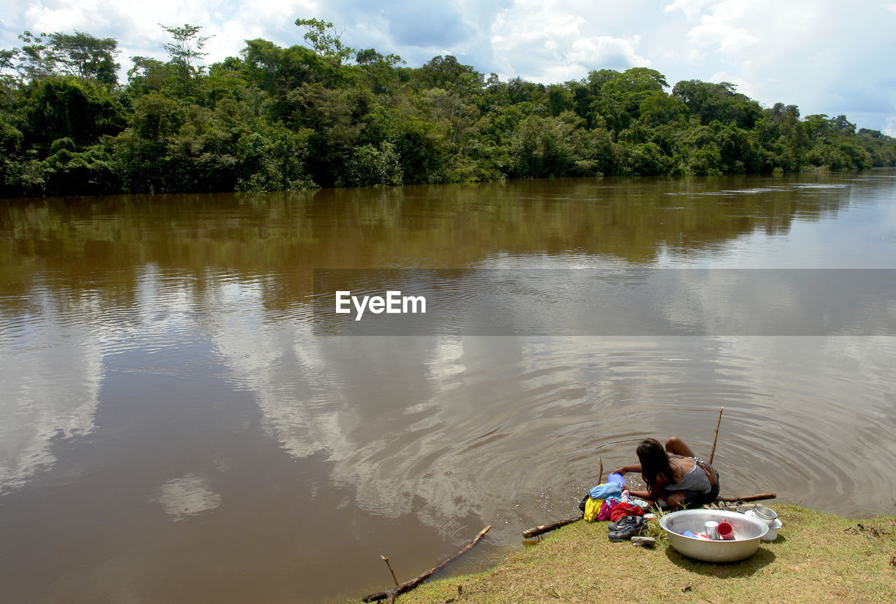 PEOPLE SITTING ON LAKE AGAINST TREES