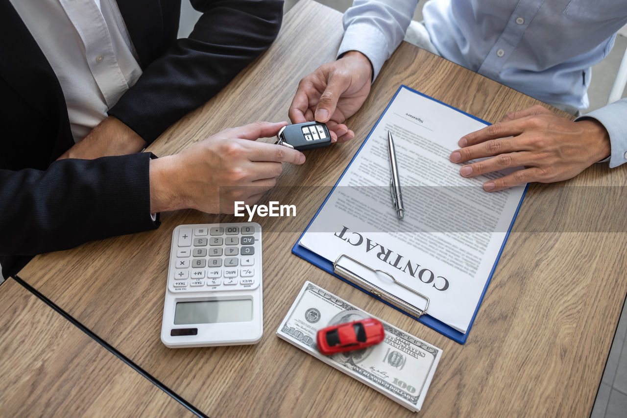 Agent giving car key to customer by papers and currency on table