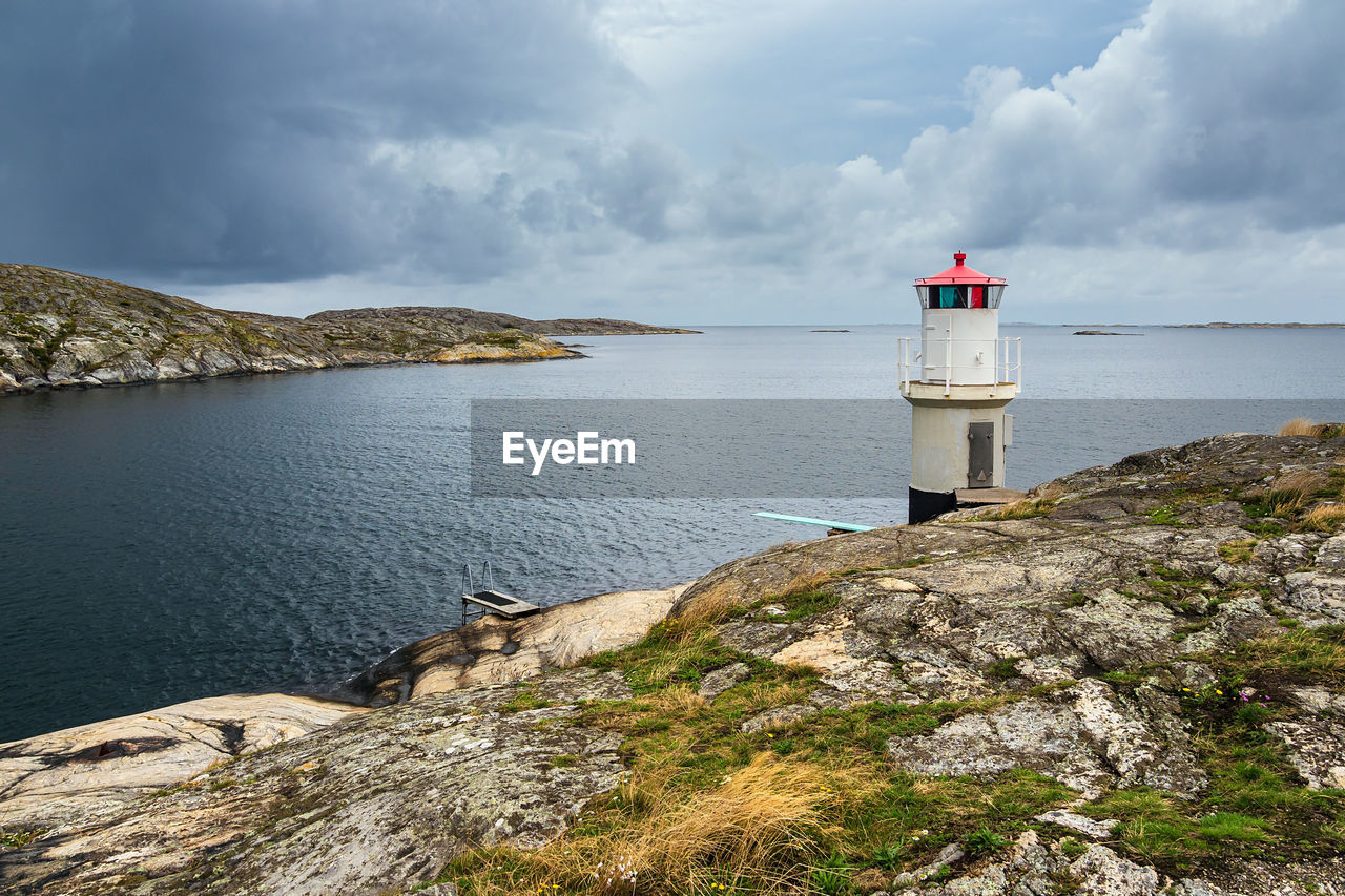 LIGHTHOUSE AMIDST ROCKS BY SEA AGAINST SKY