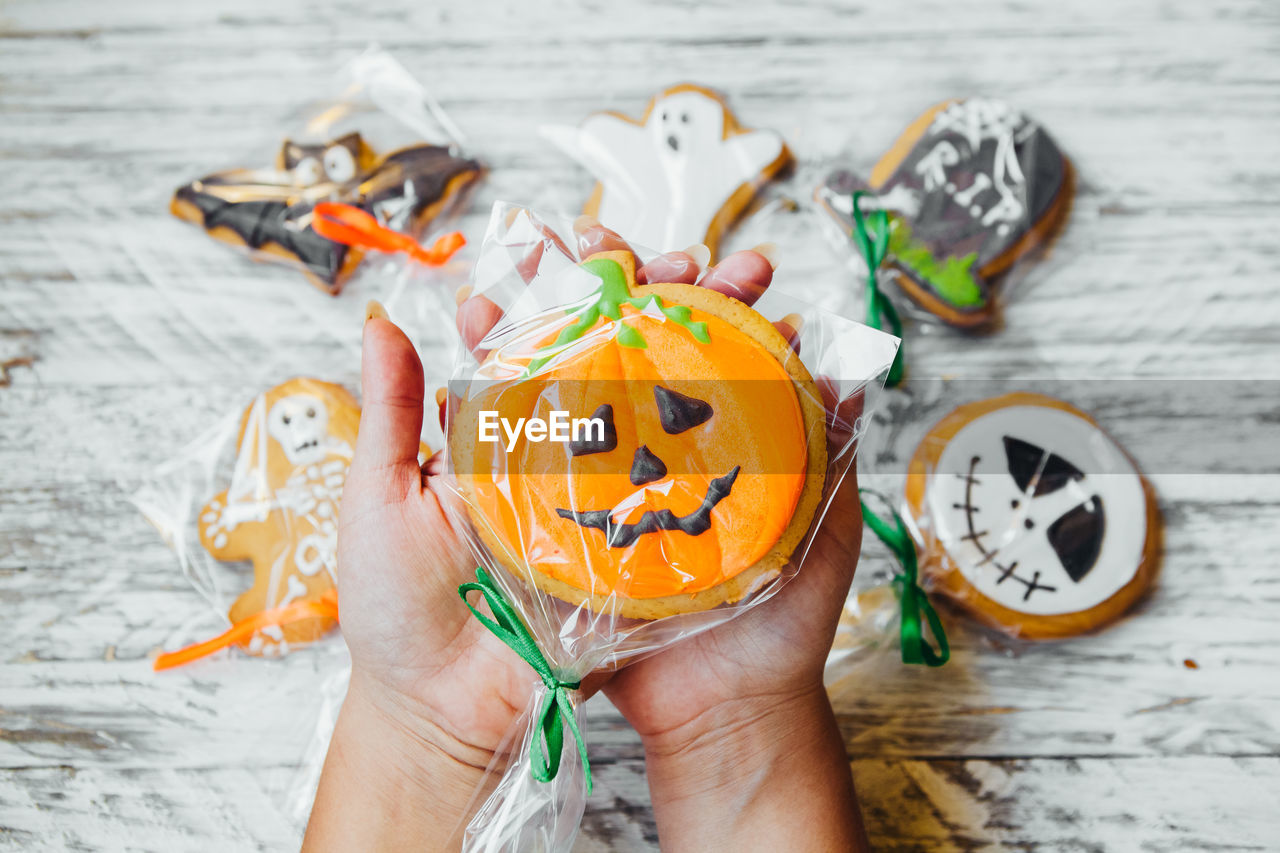 Cropped hands of woman holding various cookies wrapped in plastic over wooden table during halloween