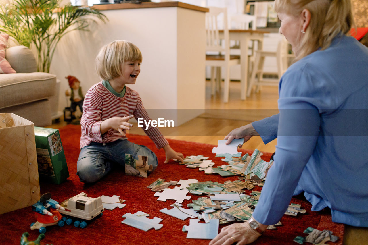 Cheerful boy playing jigsaw puzzle with grandmother in living room