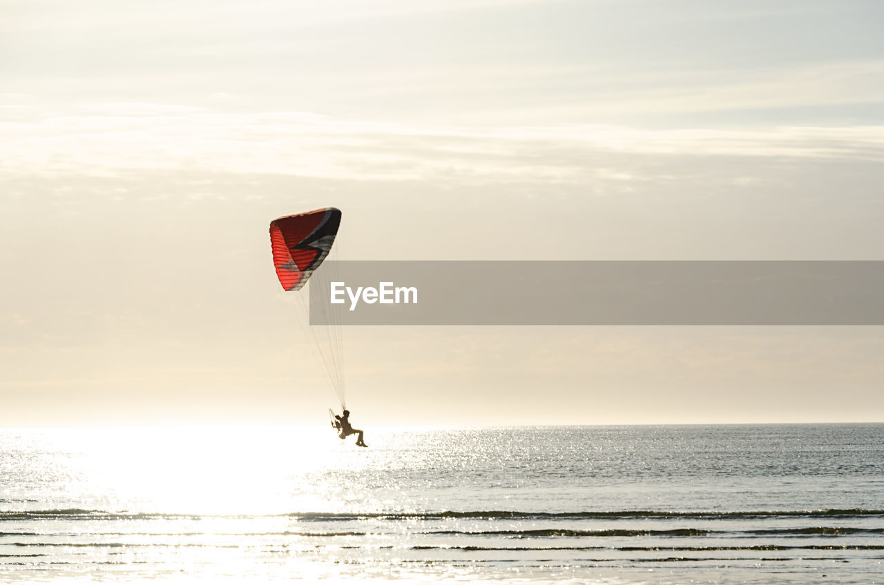 Man paragliding over sea against sky during sunset