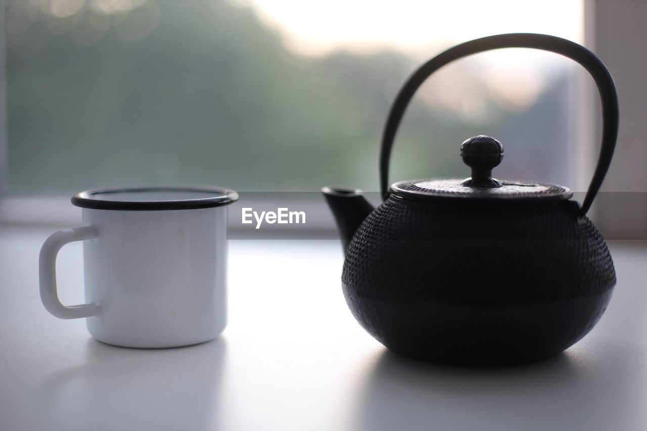 teapot, kettle, tea, hot drink, food and drink, drink, cup, mug, tea cup, indoors, no people, tea kettle, refreshment, ceramic, household equipment, tableware, still life, food, kitchen utensil, stovetop kettle, crockery, simplicity, table, nature, handle, black, steam, close-up, focus on foreground, lighting, domestic room