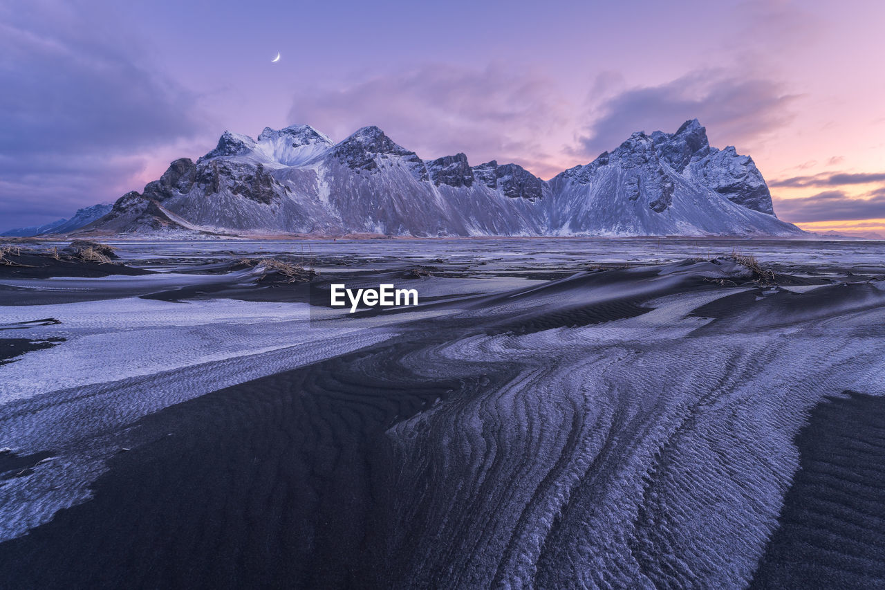 Spectacular nordic scenery of calm frozen lake near rocky vestrahorn mountain with snowy peaks during colorful sunset at stockness beach, iceland