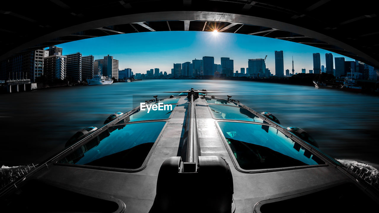 Boat in river below bridge in city