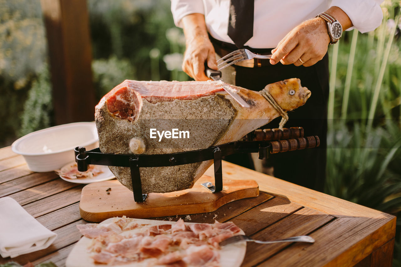 Midsection of man slicing meat outdoors