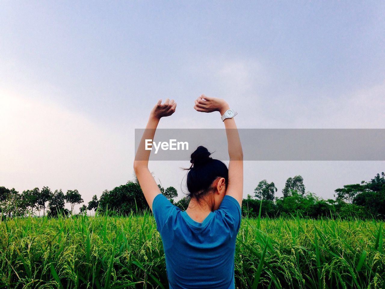 Rear view of woman standing by grassy field against sky