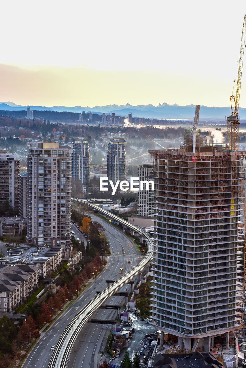 HIGH ANGLE VIEW OF ROAD BY BUILDINGS AGAINST SKY