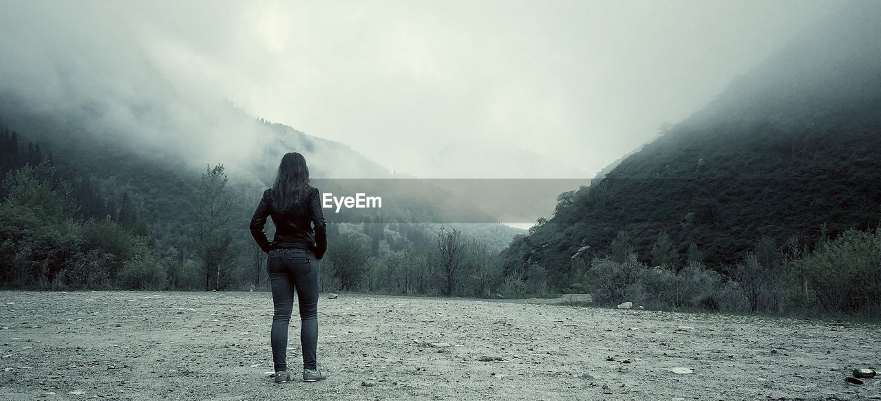 Rear view of woman standing against mountains during foggy weather