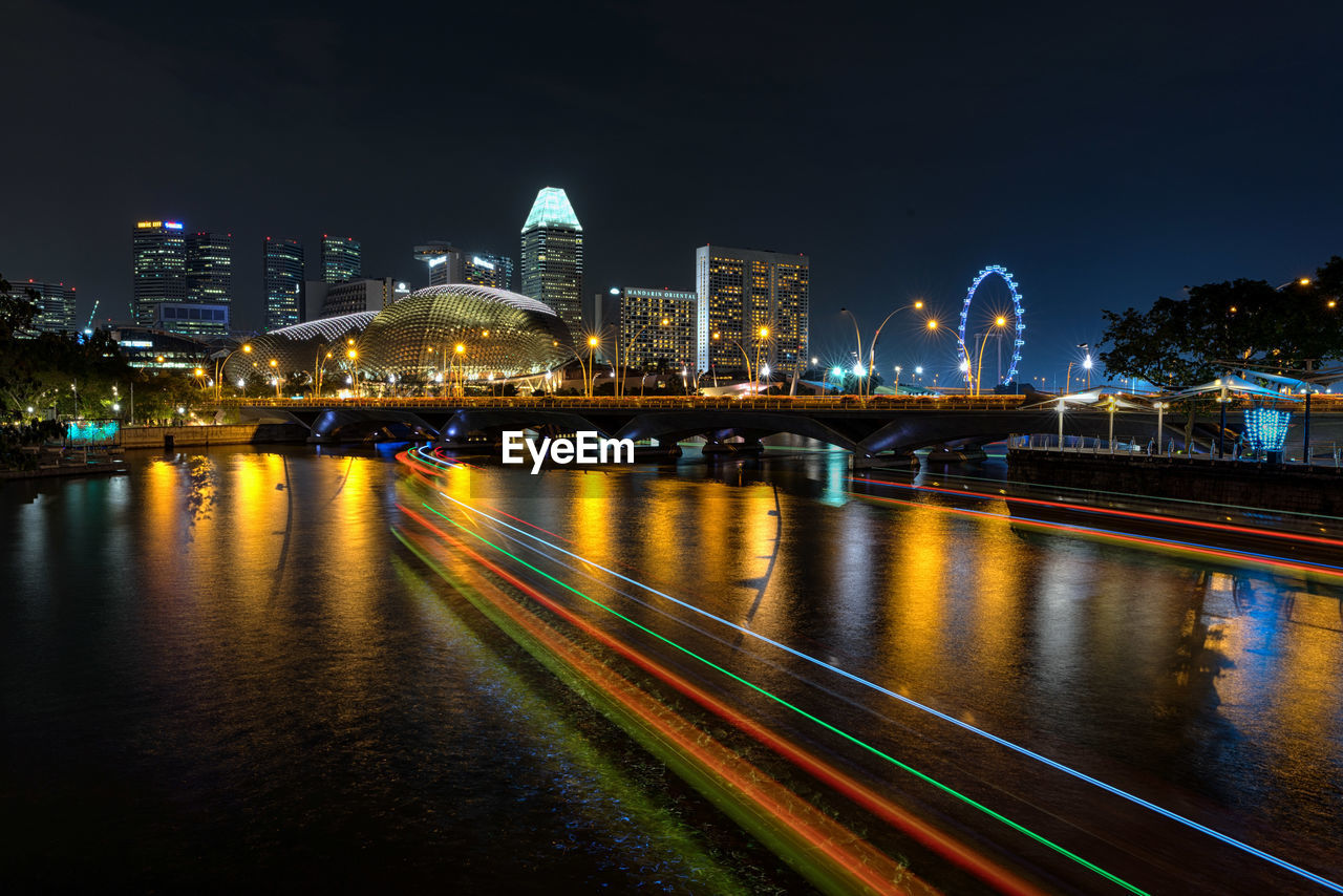 Illuminated bridge over river by buildings against sky at night