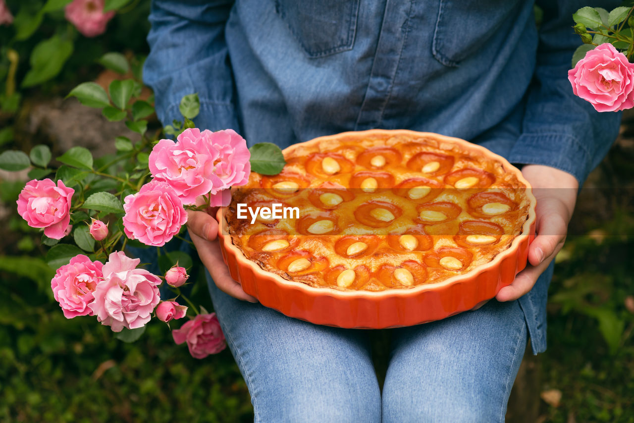 MIDSECTION OF PERSON HOLDING ICE CREAM STANDING BY PLANTS