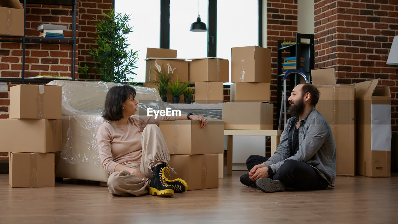 Woman sitting by boxes talking with man at home