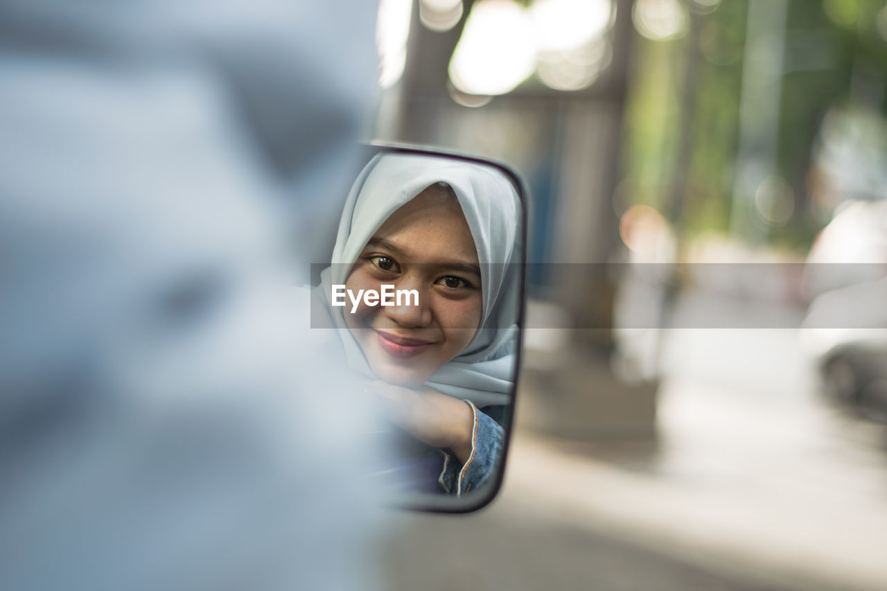 Portrait of smiling woman looking through side-view mirror