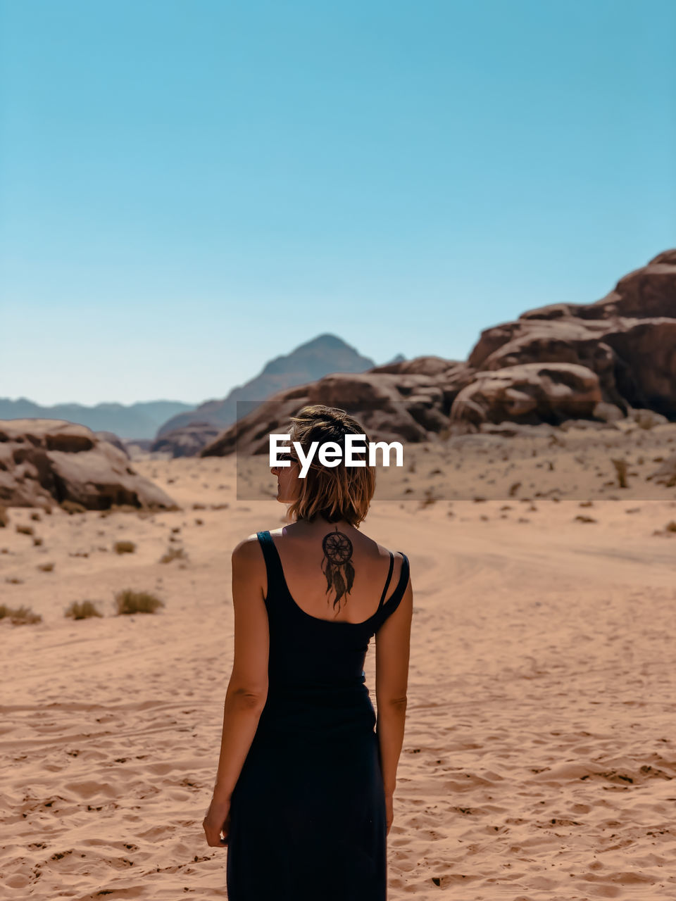 REAR VIEW OF WOMAN STANDING ON DESERT