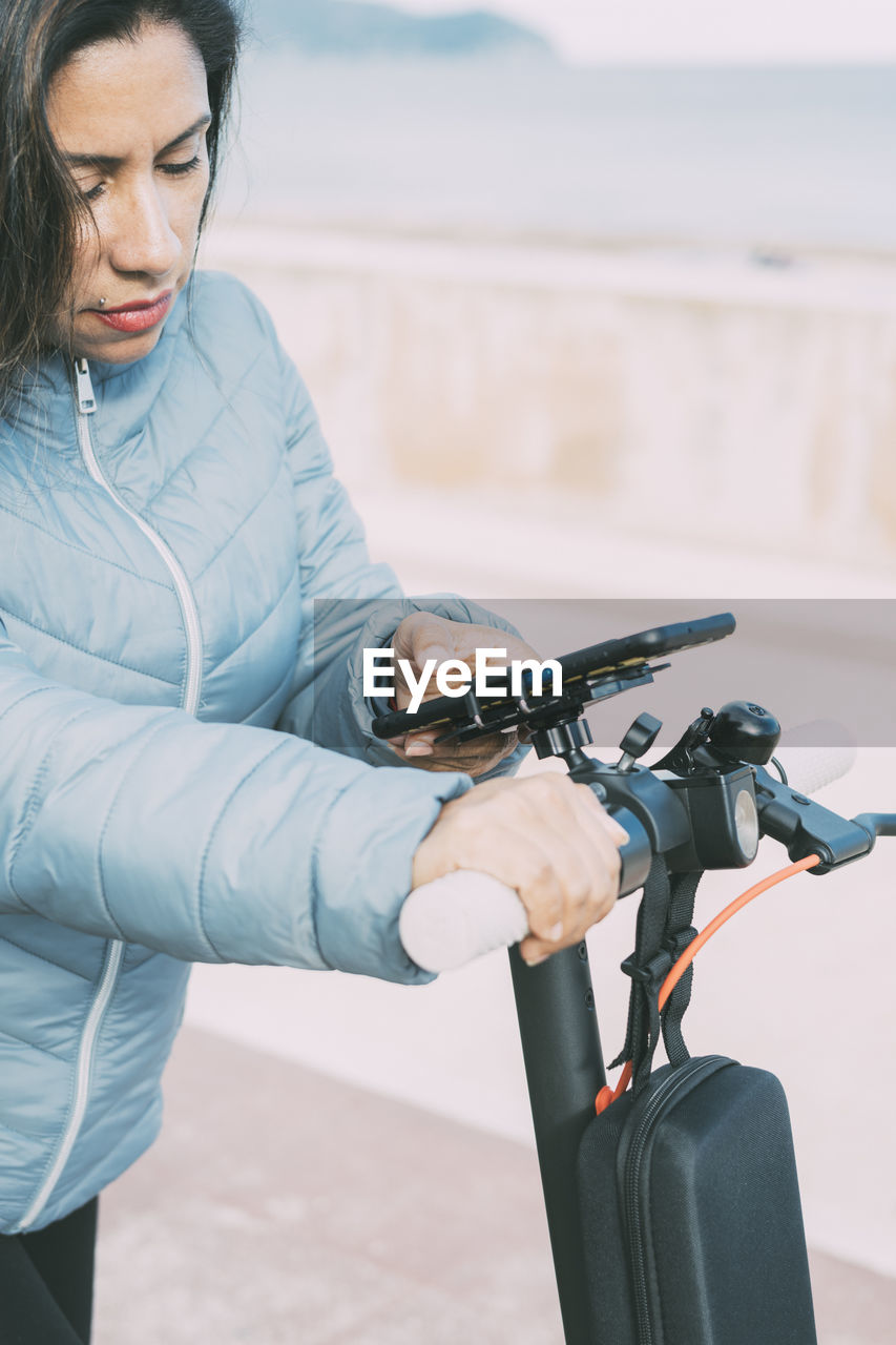 Beautiful latina woman riding her motorized scooter in the city, activating smart phone app.