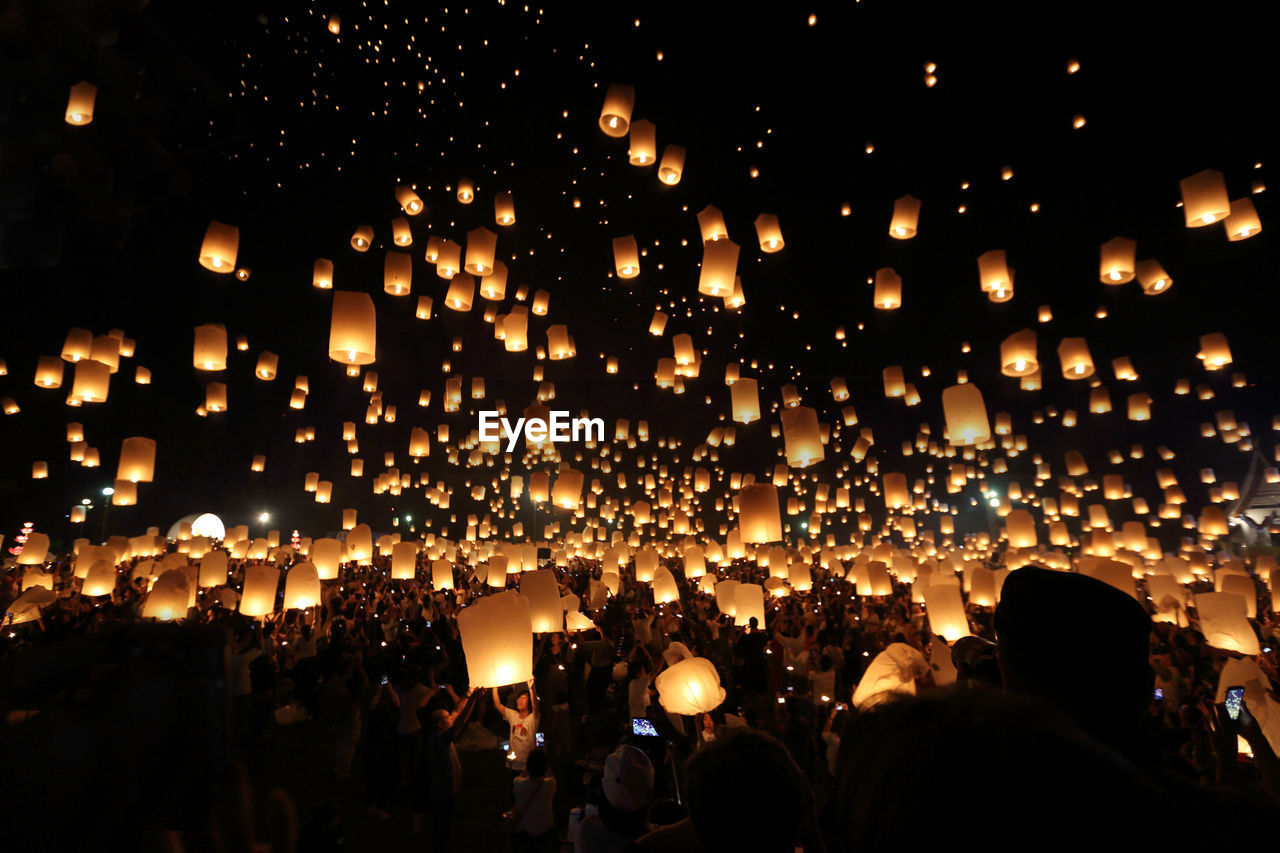 People with illuminated lanterns against sky at night