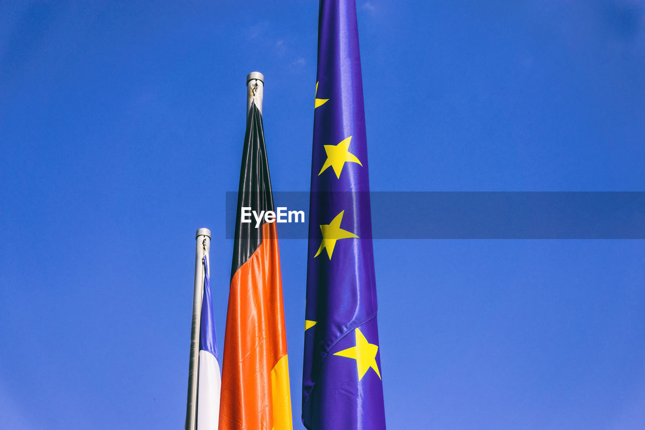 Low angle view of flags against clear blue sky during sunny day