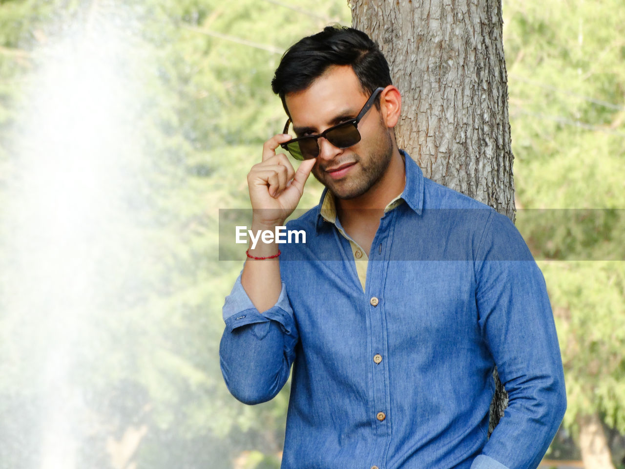 Portrait of man wearing sunglasses while leaning on tree trunk