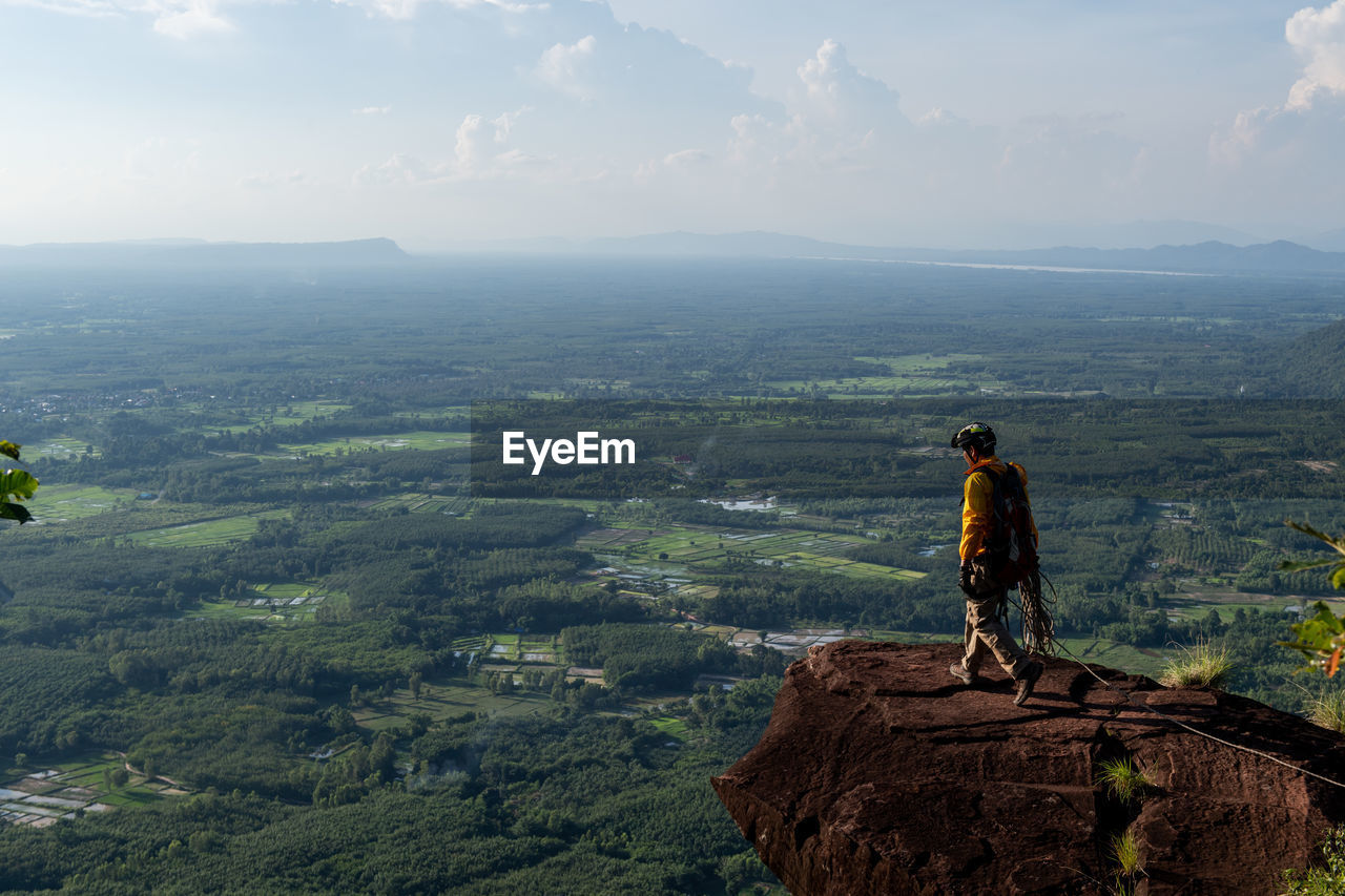 MAN STANDING ON ROCK AGAINST LANDSCAPE