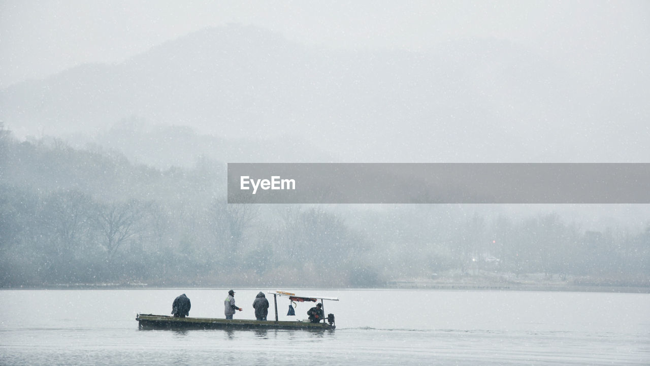 People in snow on lake against sky during foggy weather