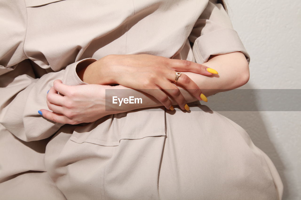 Midsection of female couple holding hands with blue and yellow manicures. wearing beige clothes 