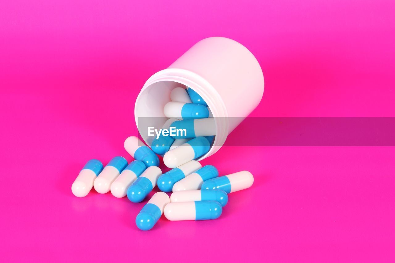 High angle view of capsules in container over pink background