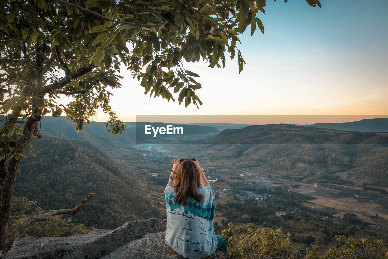 Rear view of woman photographing mountains against sky