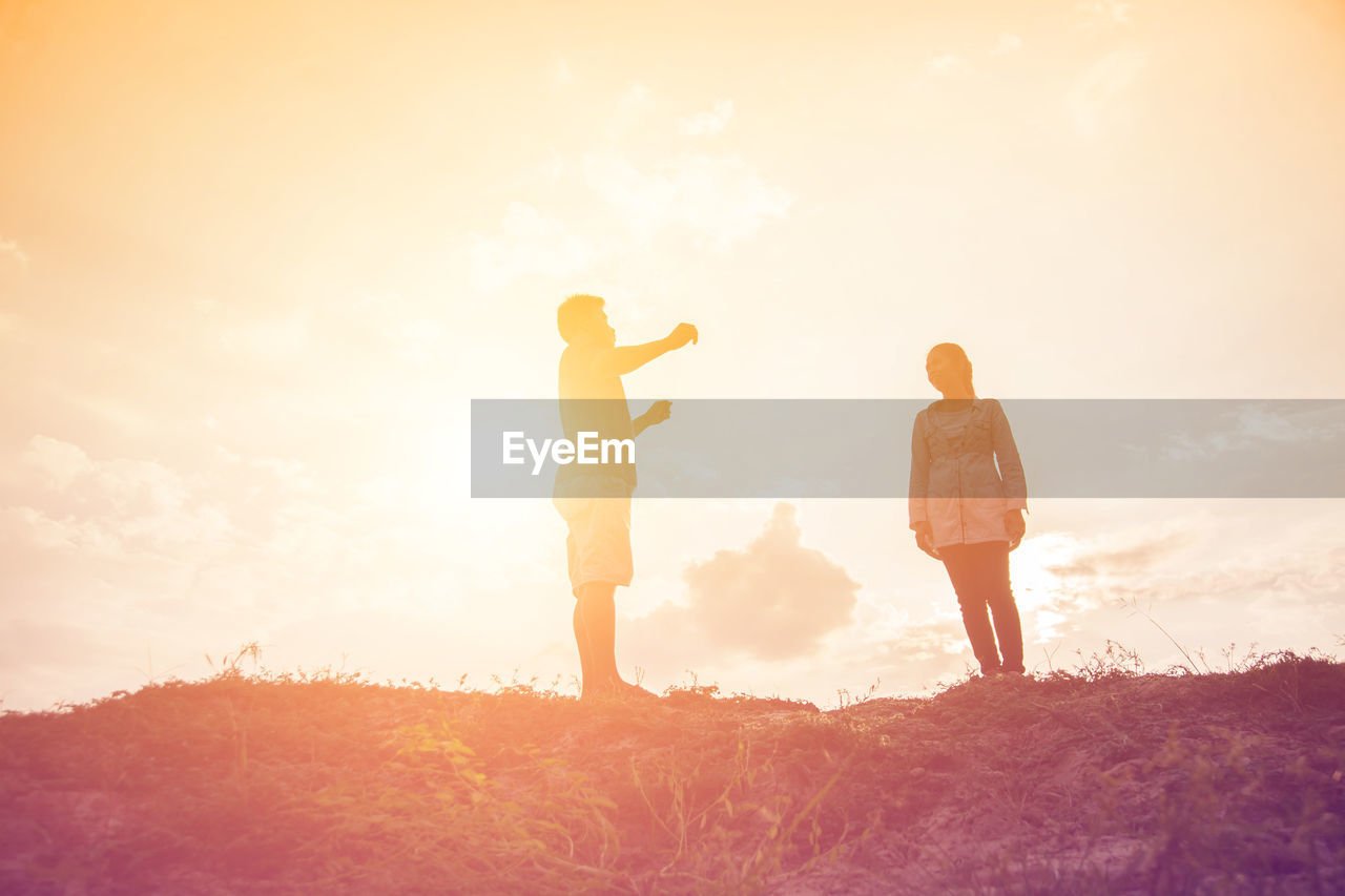 REAR VIEW OF MAN AND WOMAN STANDING ON FIELD AGAINST SKY