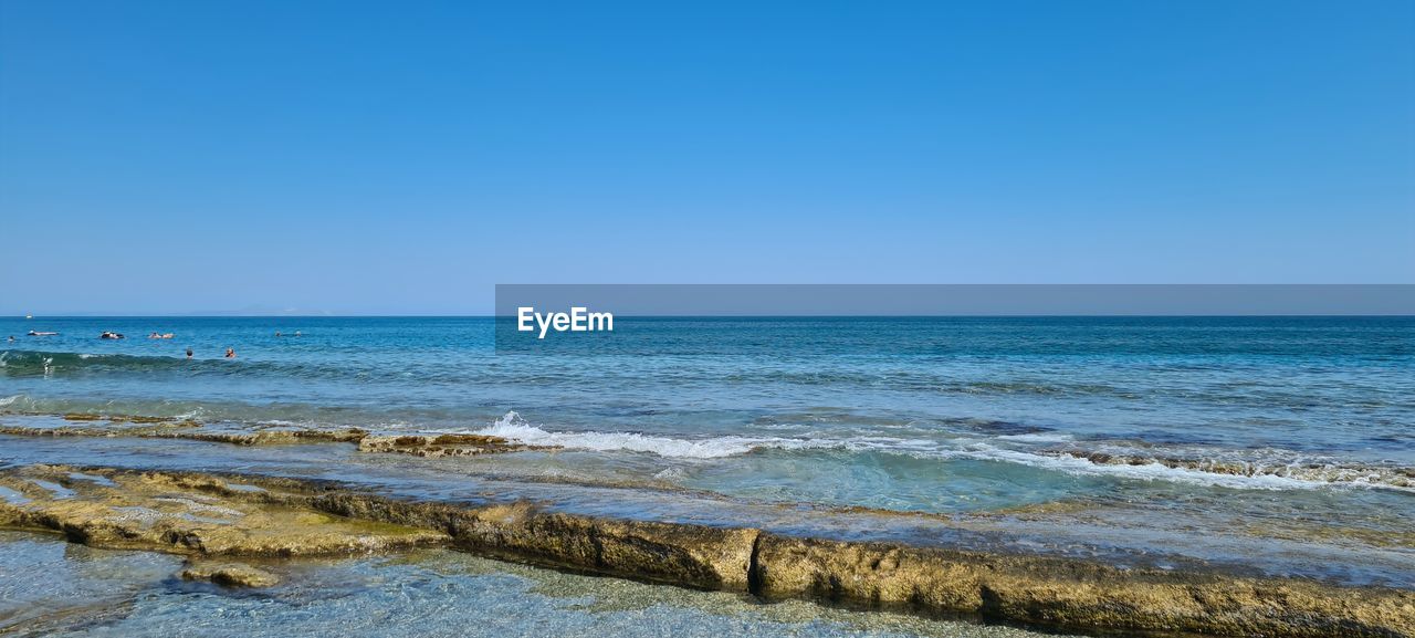 sea, water, land, sky, beach, body of water, horizon, scenics - nature, horizon over water, beauty in nature, shore, wave, ocean, clear sky, nature, blue, wind wave, tranquility, coast, tranquil scene, no people, sand, vacation, day, motion, idyllic, travel destinations, travel, outdoors, copy space, sunny, tourism, environment, water sports, sports, non-urban scene, rock, seascape, bay, terrain, sunlight, cliff