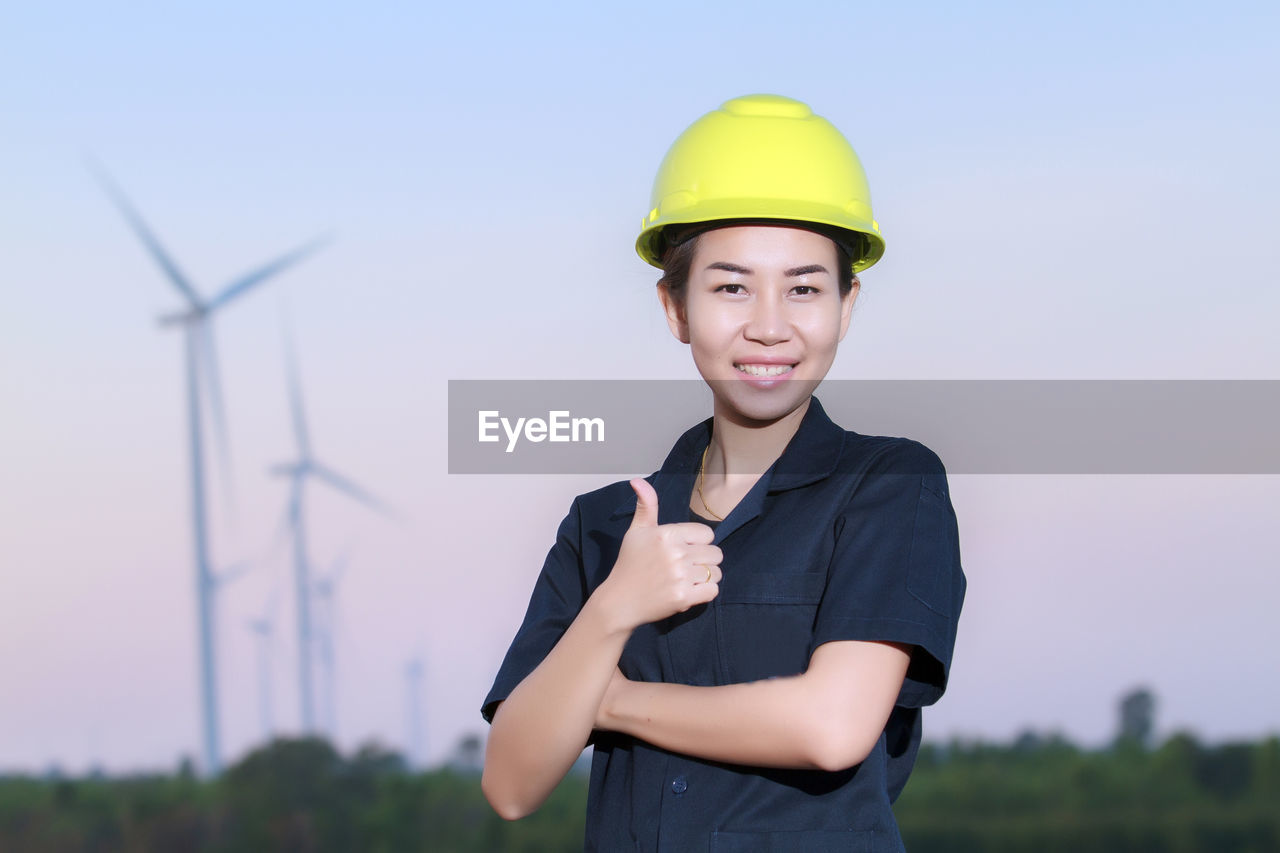 Portrait of engineer holding blueprint against sky