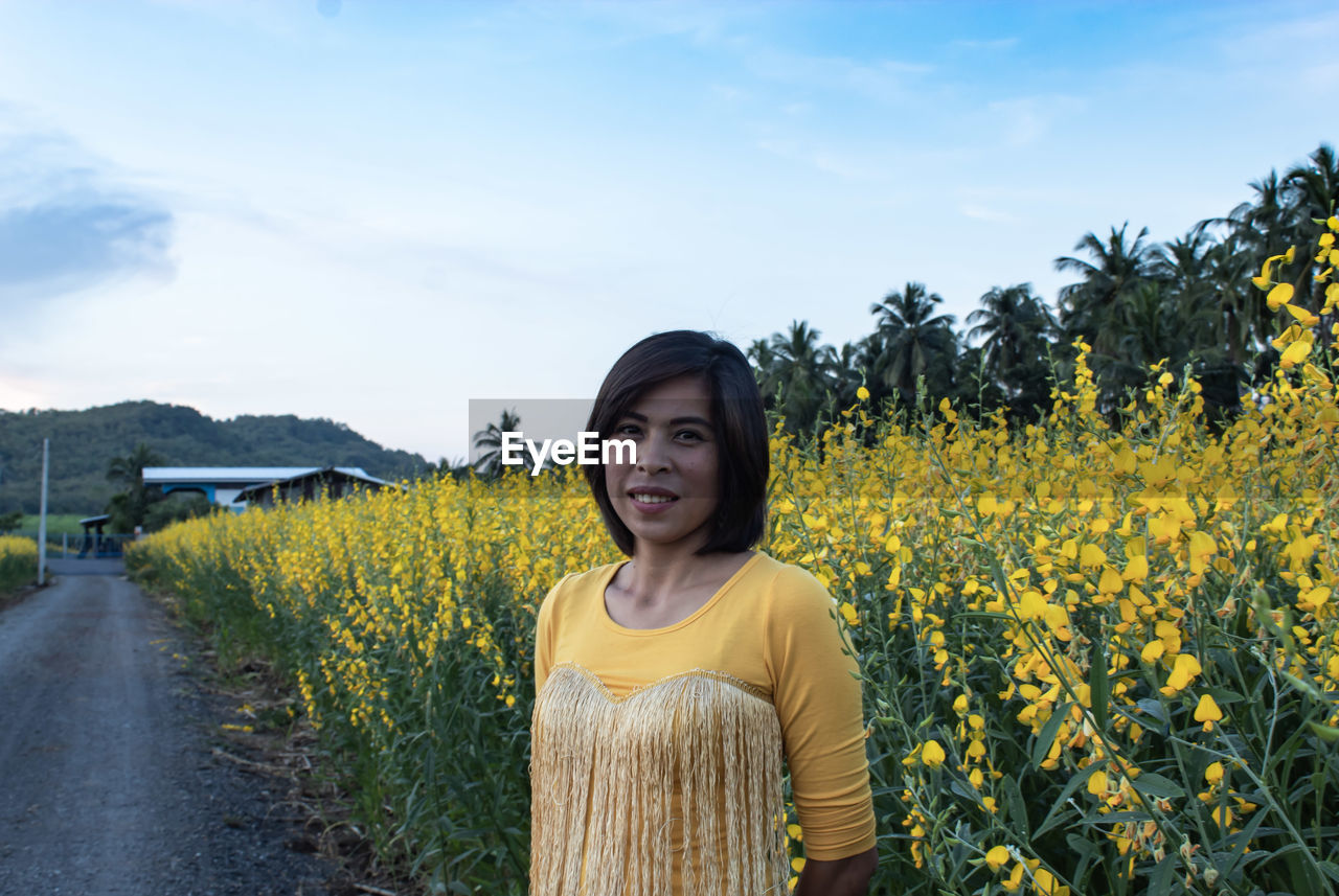 Portrait of woman standing against yellow flowering plants