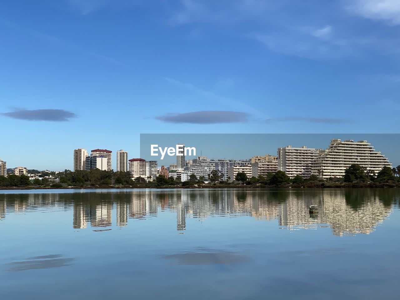 Reflection of buildings in lake against blue sky