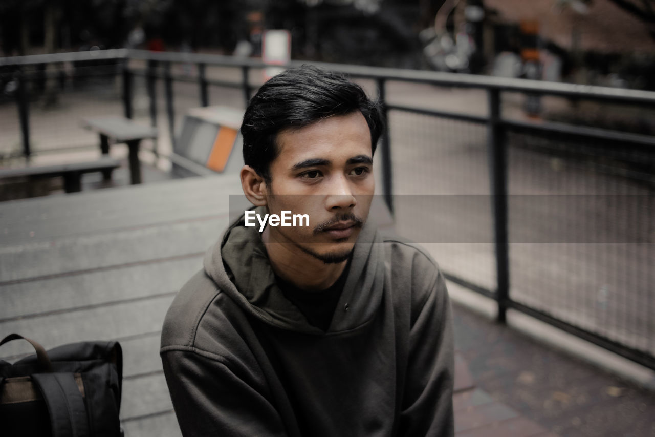 Portrait of young man sitting on railing