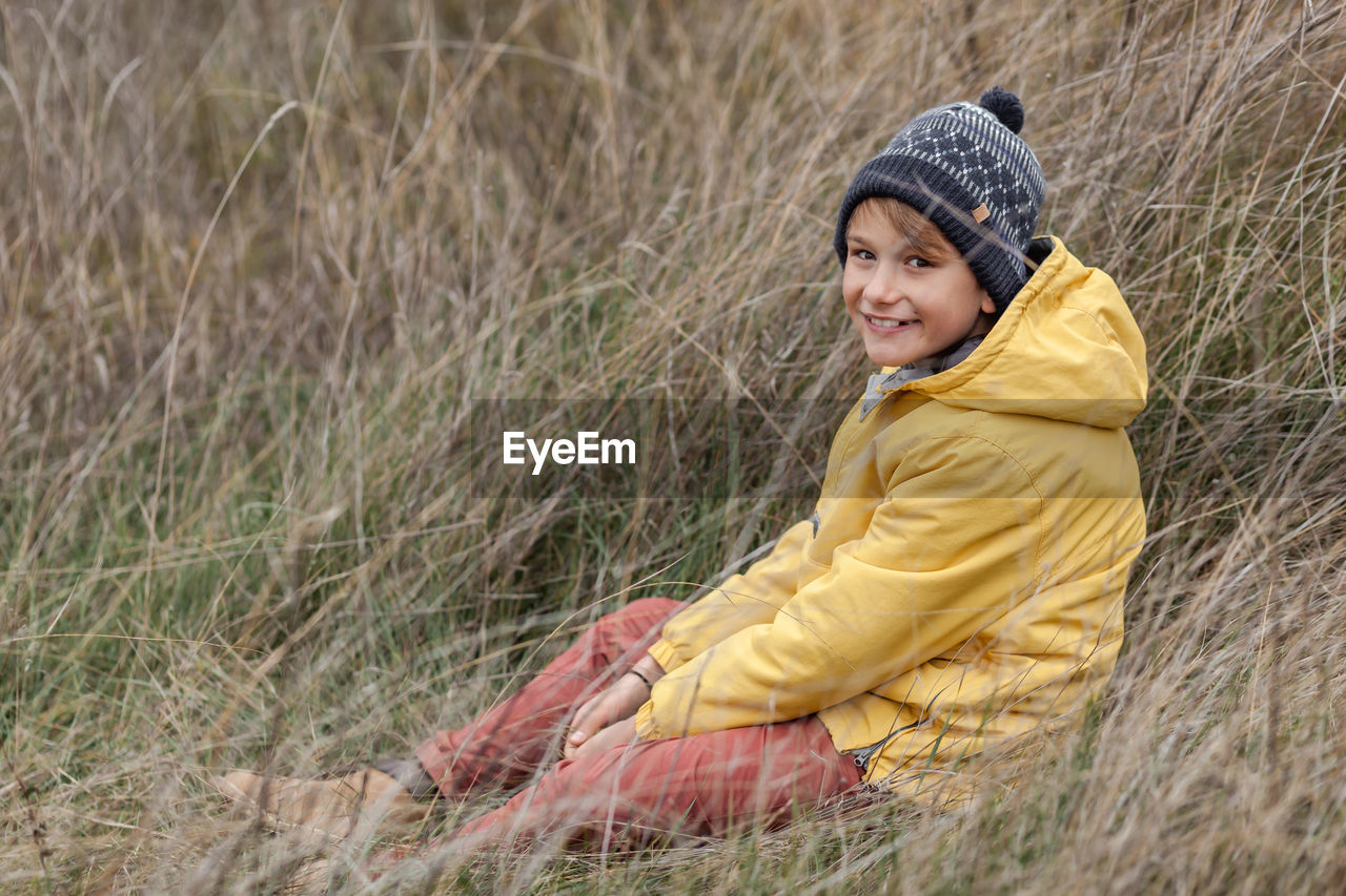 Happy boy relaxing in tall grass during autumn day and looking at camera. copy space.