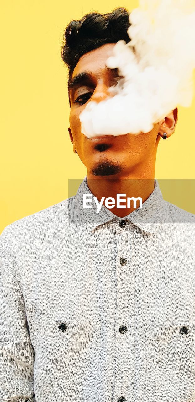 Portrait of young man smoking against yellow background