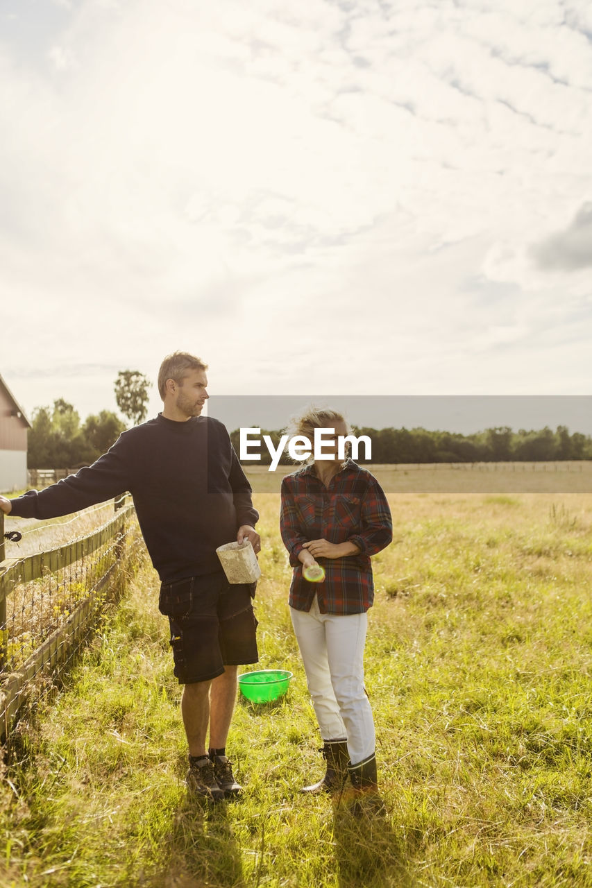 Man and woman talking while standing on grassy field against sky