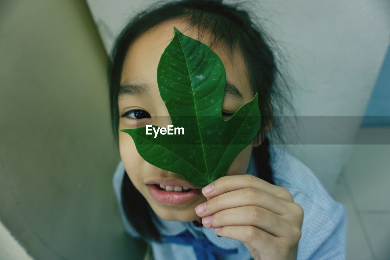 Close-up high angle portrait of girl covering eye with leaf