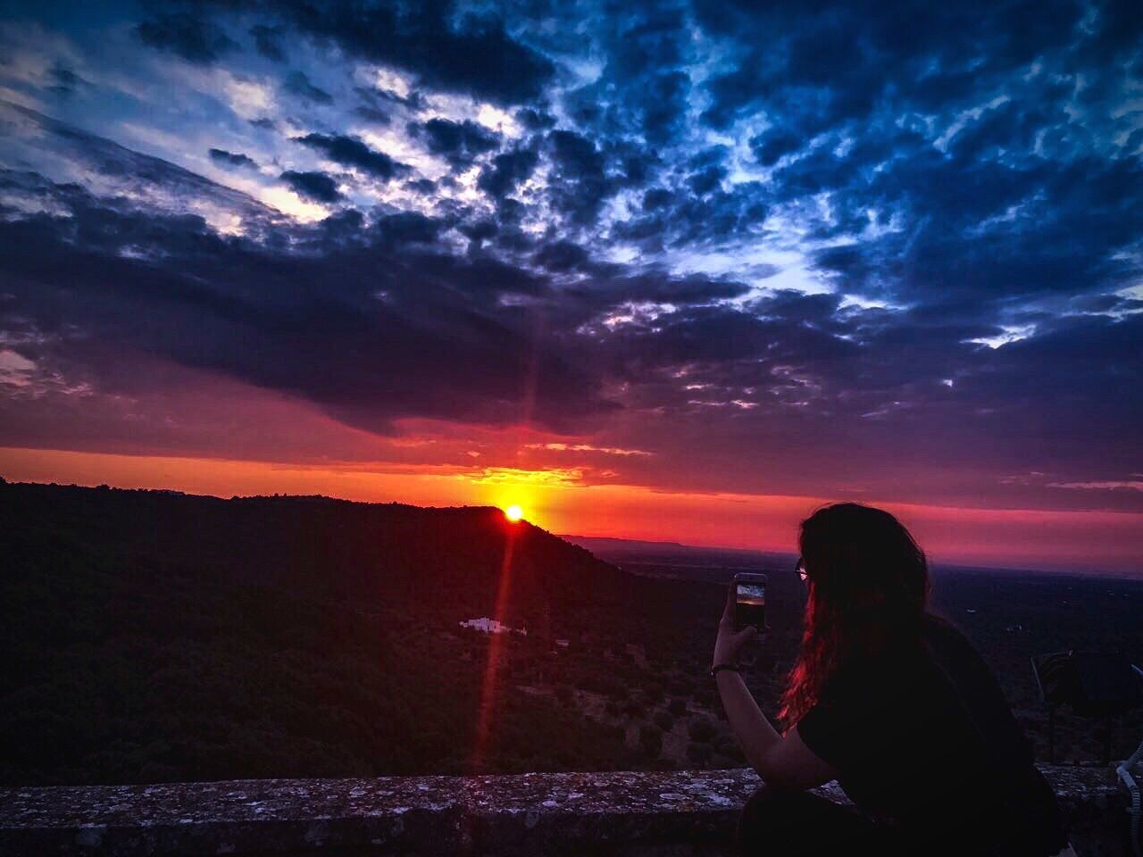 SIDE VIEW OF WOMAN PHOTOGRAPHING AT SUNSET SKY