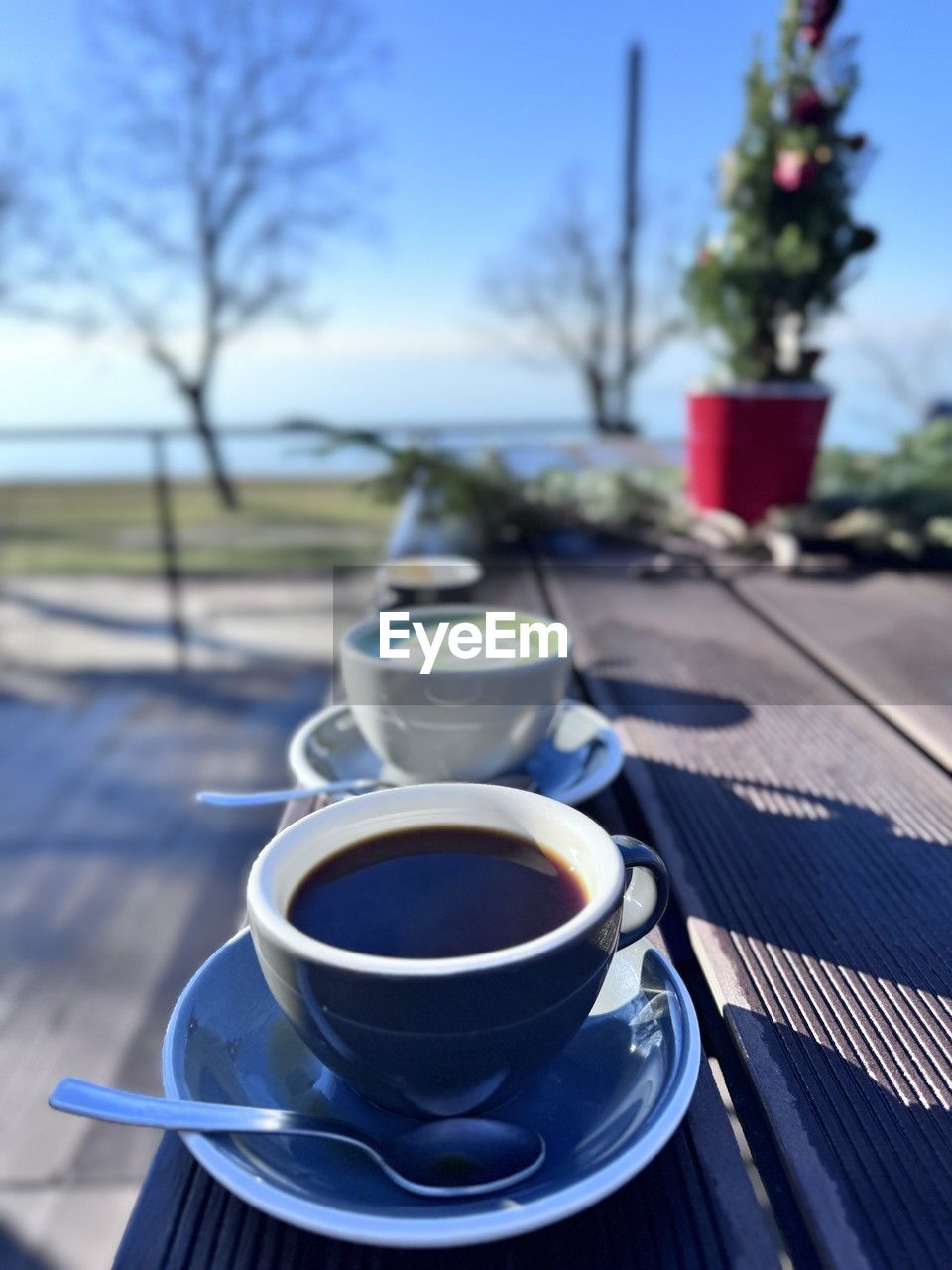 food and drink, drink, refreshment, cup, blue, mug, coffee, crockery, coffee cup, nature, saucer, table, tree, plant, day, food, focus on foreground, hot drink, no people, outdoors, sky, kitchen utensil, freshness, sunlight, tea, tableware, morning, household equipment, close-up, eating utensil, spoon, wood