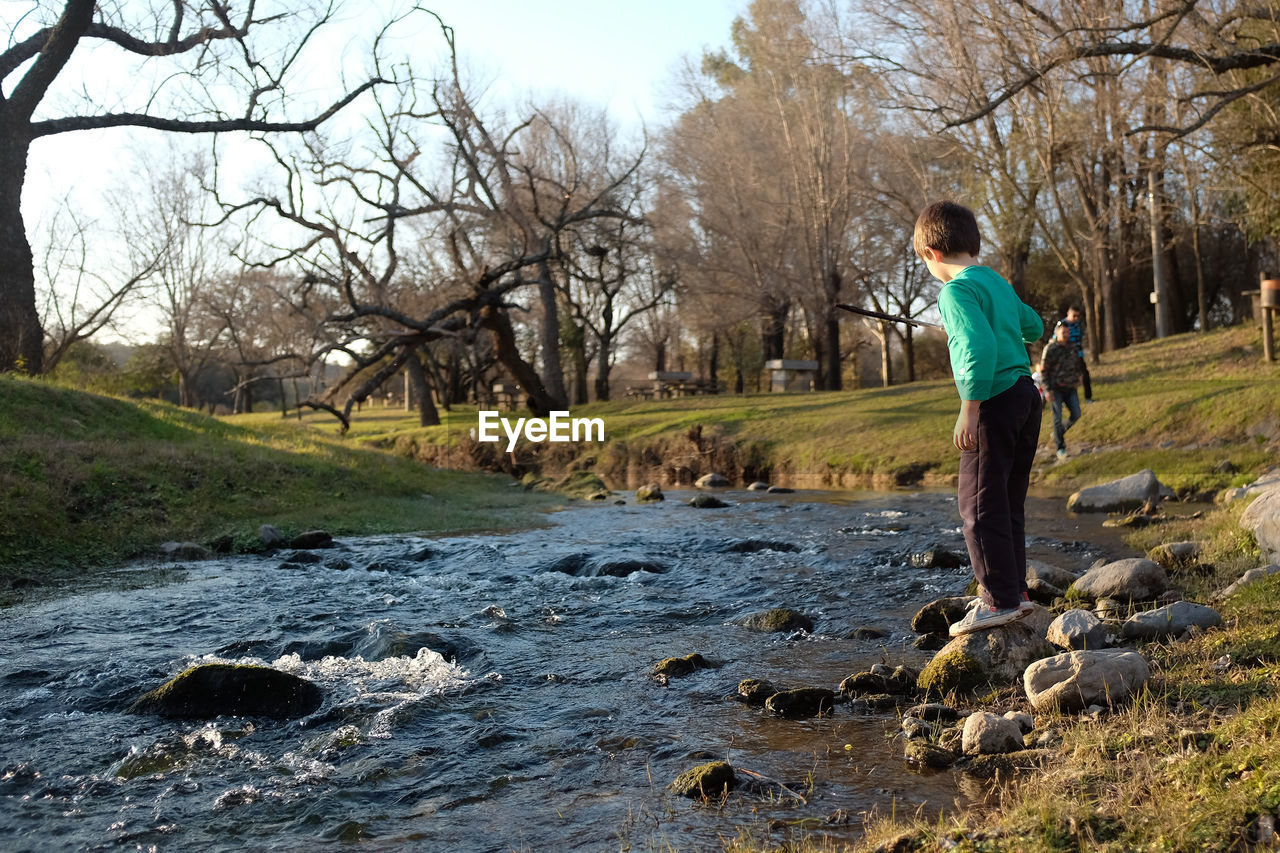 SIDE VIEW OF BOY STANDING BY PLANTS IN STREAM