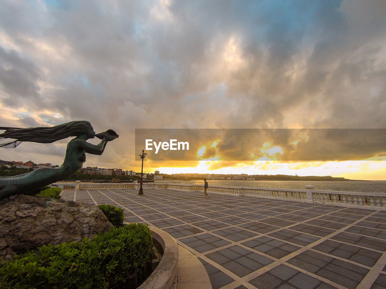 Statue of mermaid by the sea with beautiful big clouds at sunset. taken in santander, spain.