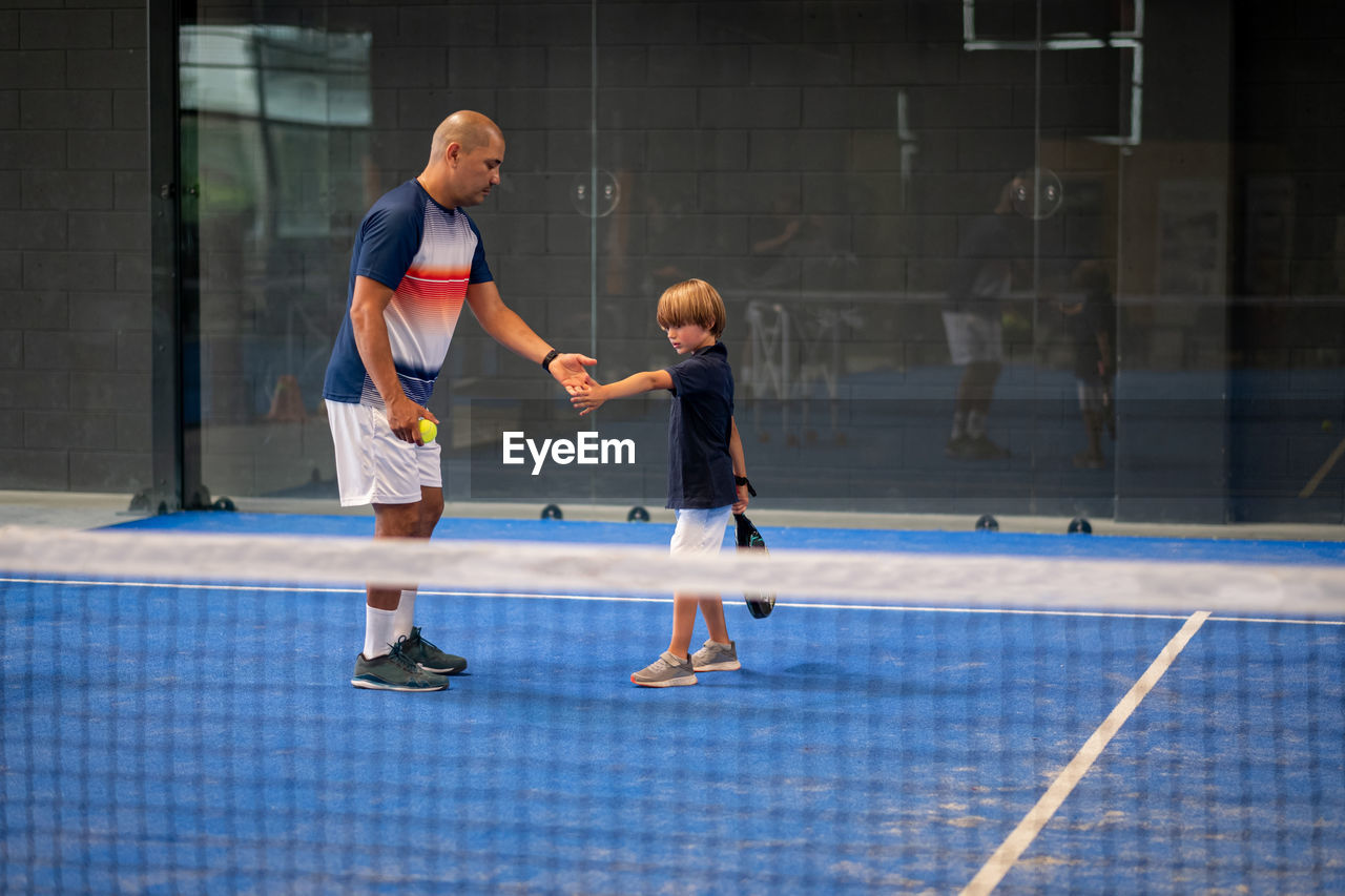 Monitor teaching padel class to child, his student - trainer teaches little boy how to play padel 