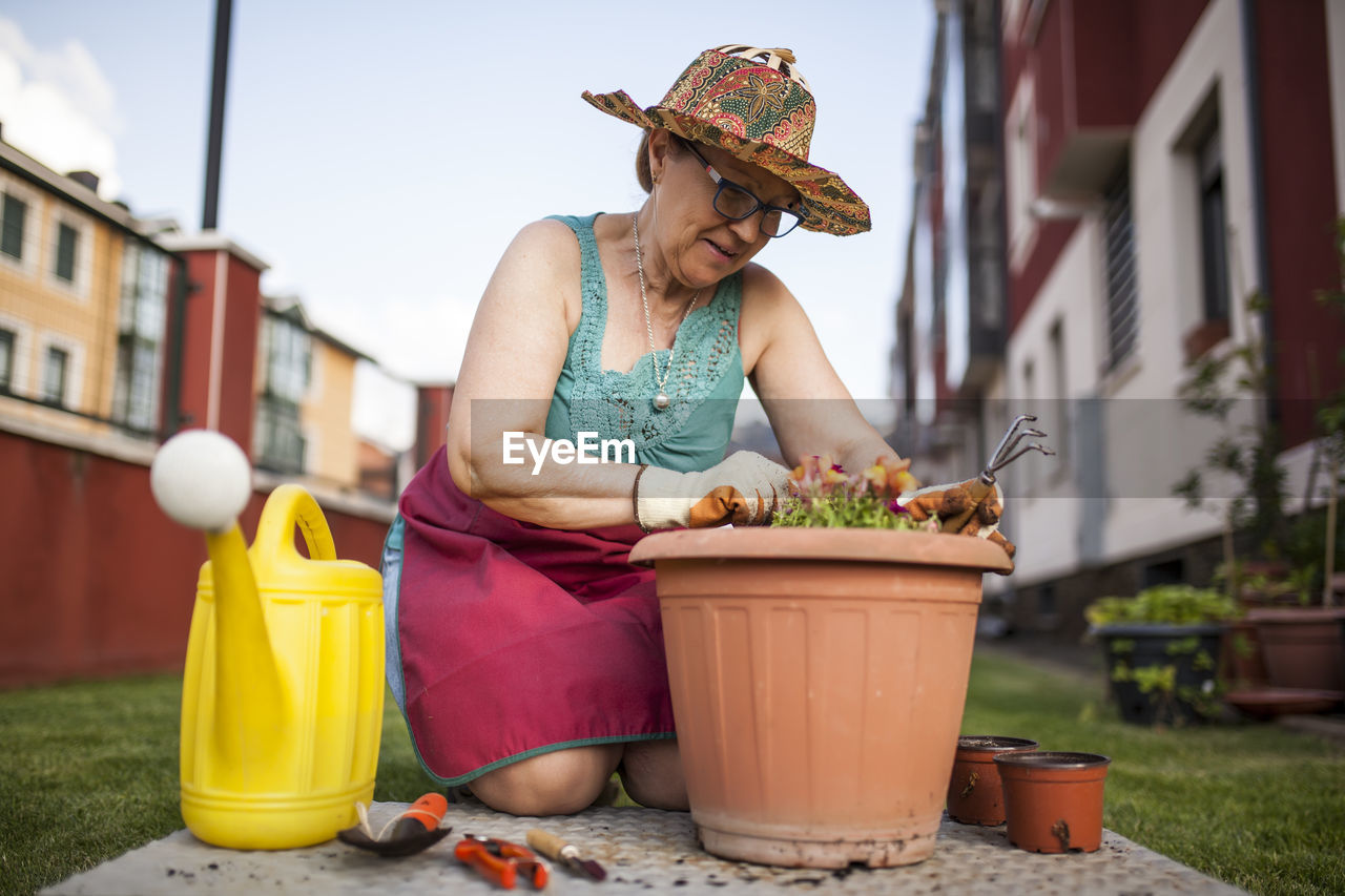 From below mature woman gardener, transfers a plant to a large flowerpot in her home garden
